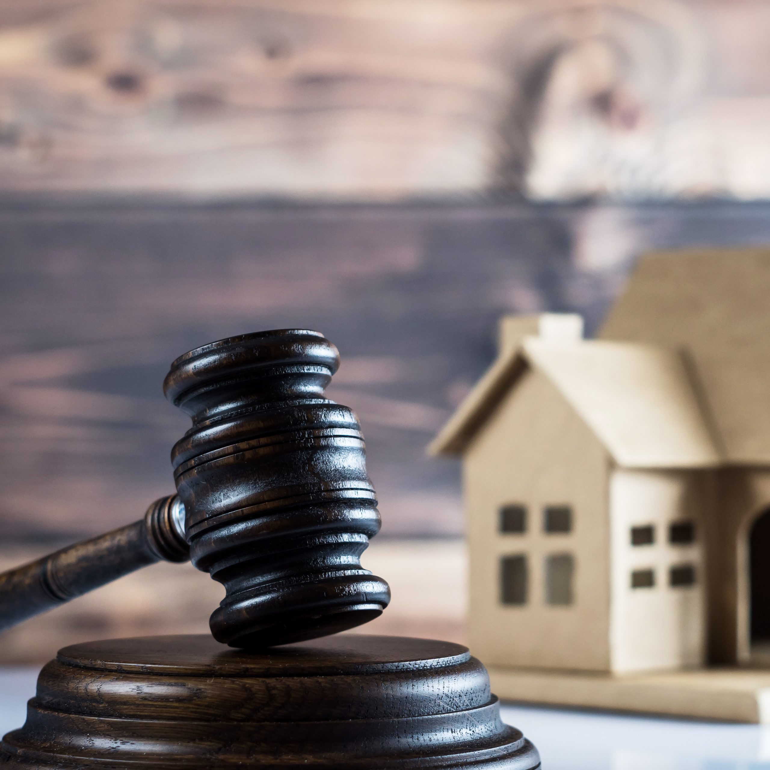 Marteau de justice posé devant une maison miniature, illustrant un litige immobilier, un contentieux locatif ou une question de droit de la construction.