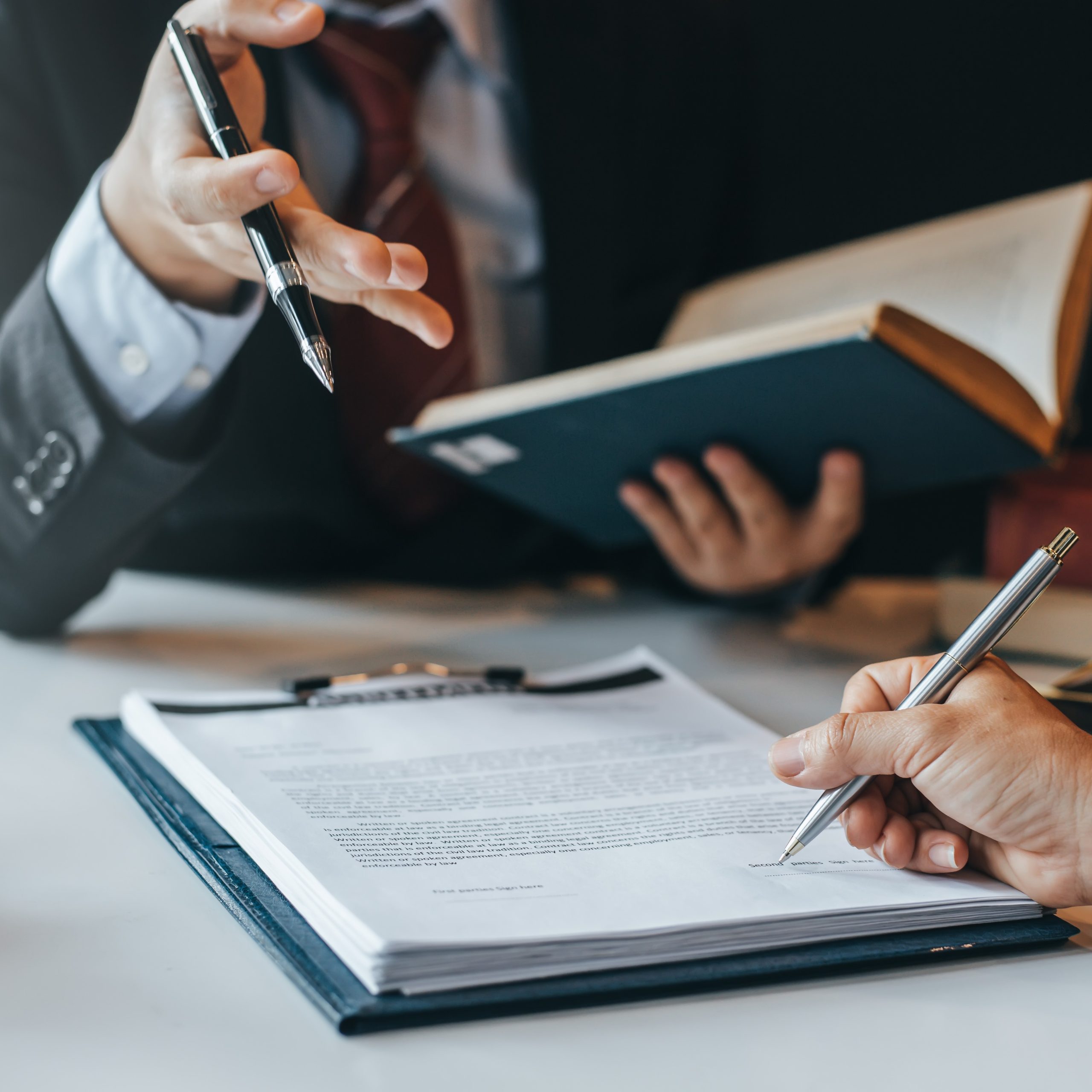 Signature d’un document lors d’une consultation juridique, avec échange entre un professionnel du droit et un client autour d’un dossier.