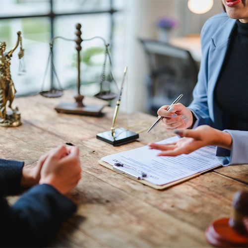 Consultation juridique entre un avocat et un client autour de documents, avec une balance de la justice visible sur le bureau.